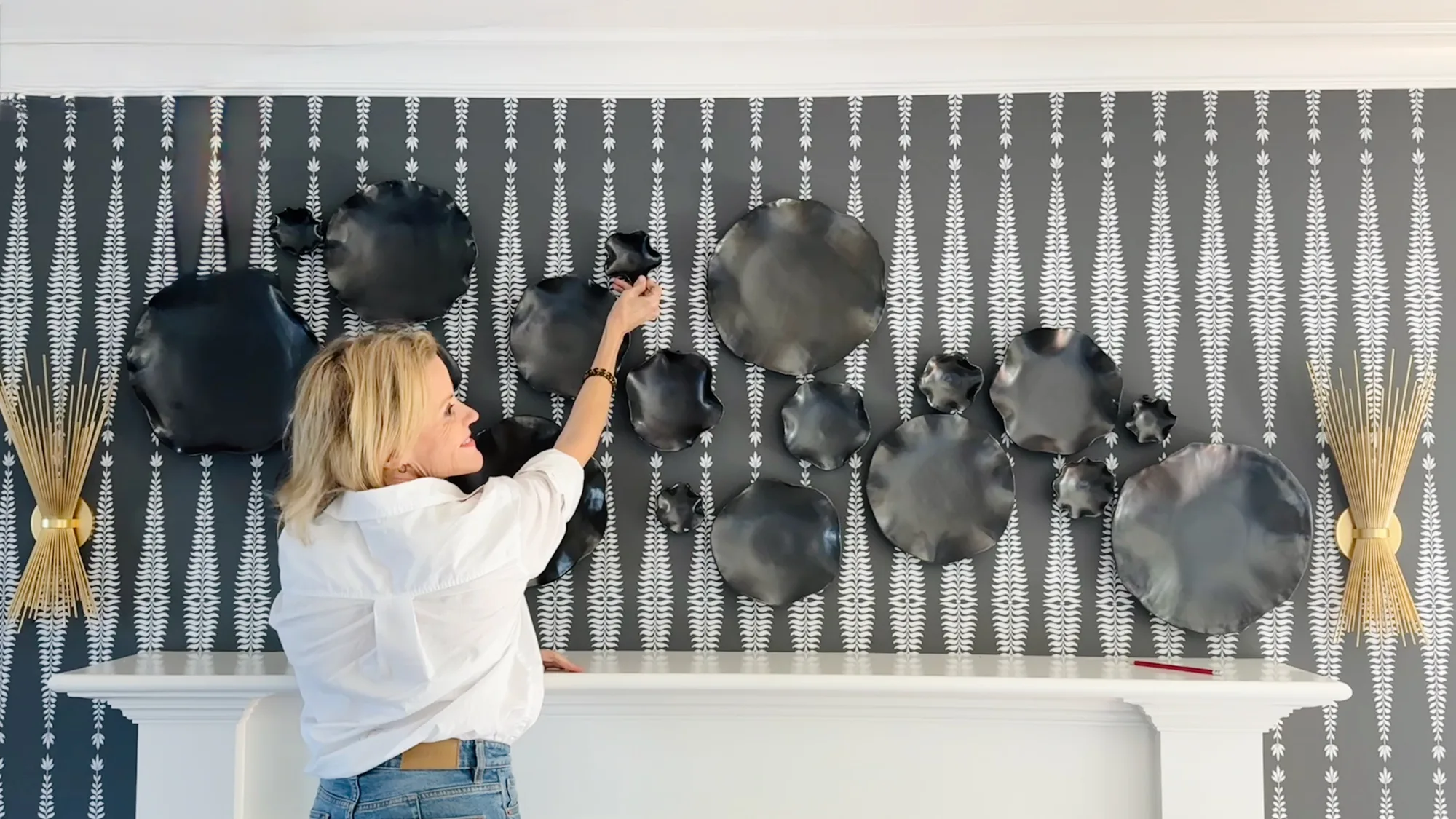 Krysta Mae hanging a wall installation of dark ruffled discs above a mantel