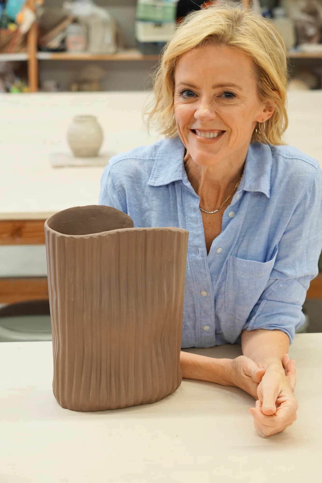 Krysta Mae at a table beside one of her tall carved sculptural vessels