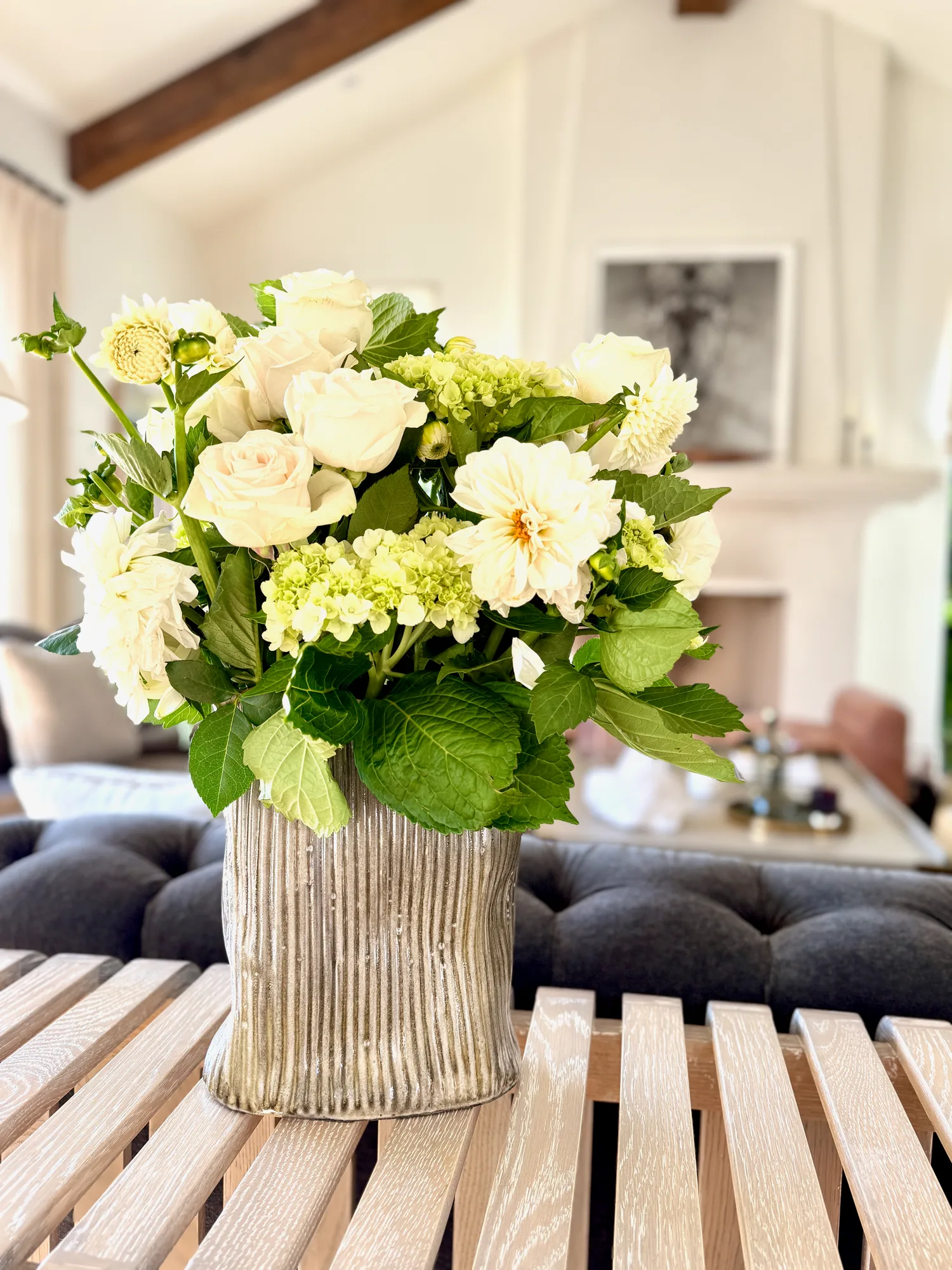 A carved Krysta Mae vessel holding white and green flowers in a living room